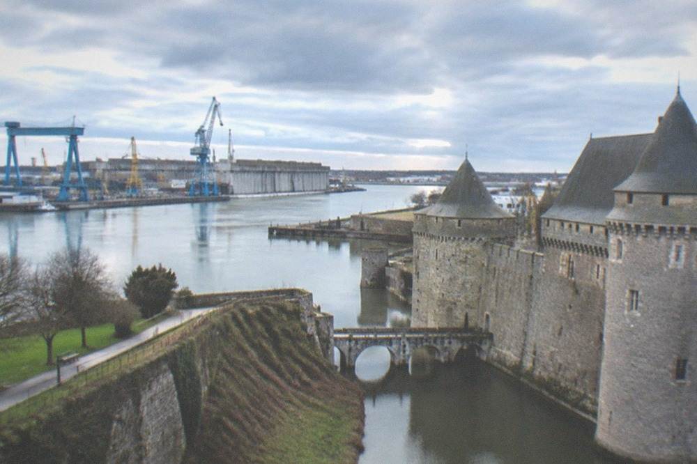 A granite castle fortress with towers and a moat in a French city centre under a blue sky