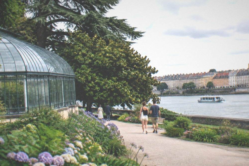 A small passenger ferry crossing a wide river toward colourful waterside houses in summer light