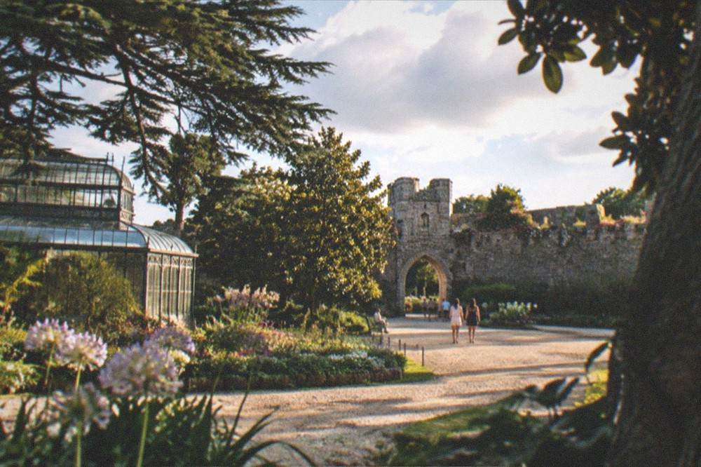 A medieval stone gateway and flower-lined ramparts under a bright blue summer sky