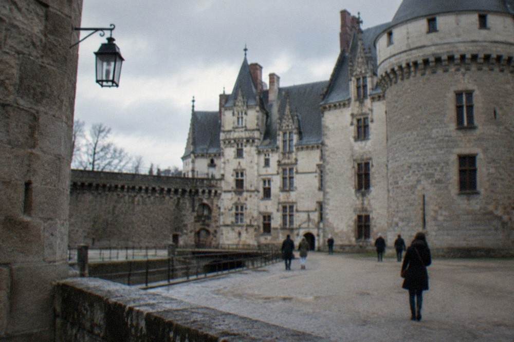 A stone castle courtyard with dark walls and a few visitors in coats under a grey sky