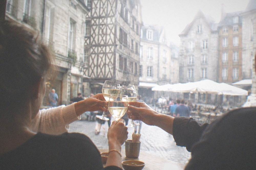 Friends toasting with glasses of white wine at a wooden bar counter