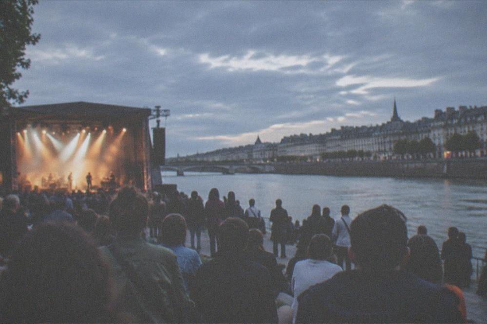 Open-air concert crowd gathered along a riverbank at dusk in Nantes