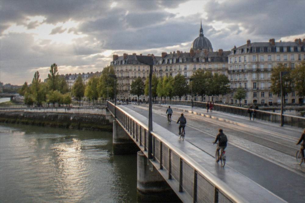 Cyclists crossing an illuminated bridge over the Loire in Nantes in the early evening