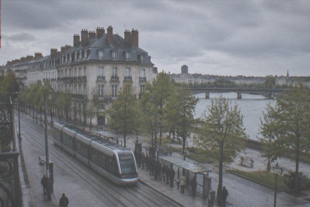 A Naolib tram passing through a Nantes street with passengers waiting at the stop