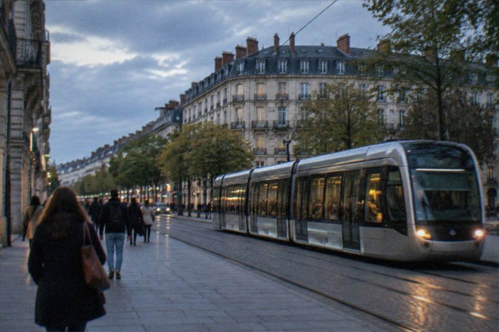 A modern tram passing along a Nantes street with pedestrians on a wide pavement