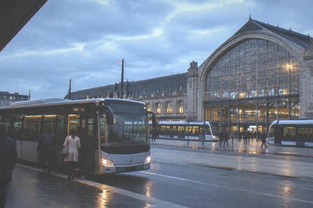 A shuttle bus parked at a kerb outside a railway station with passengers boarding