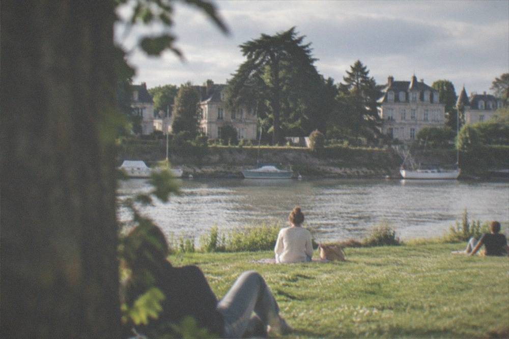 People relaxing on a sunny lawn beside the Erdre river in Nantes