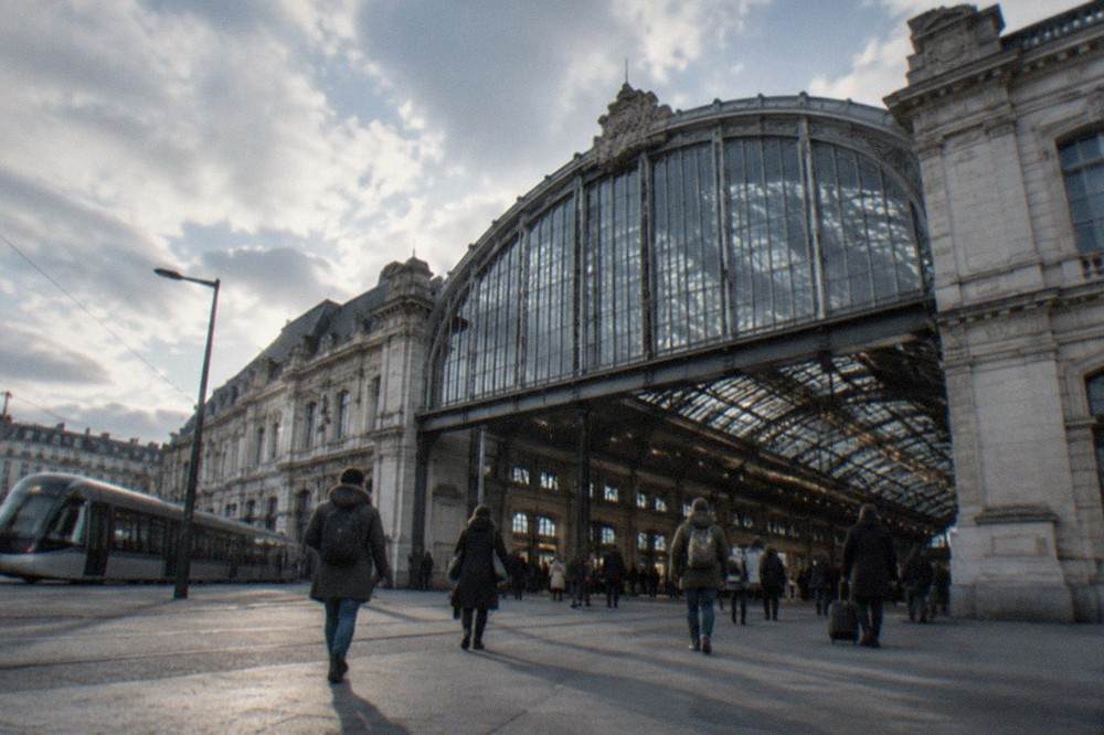 Passengers walking through a large rail station concourse with a departure board overhead