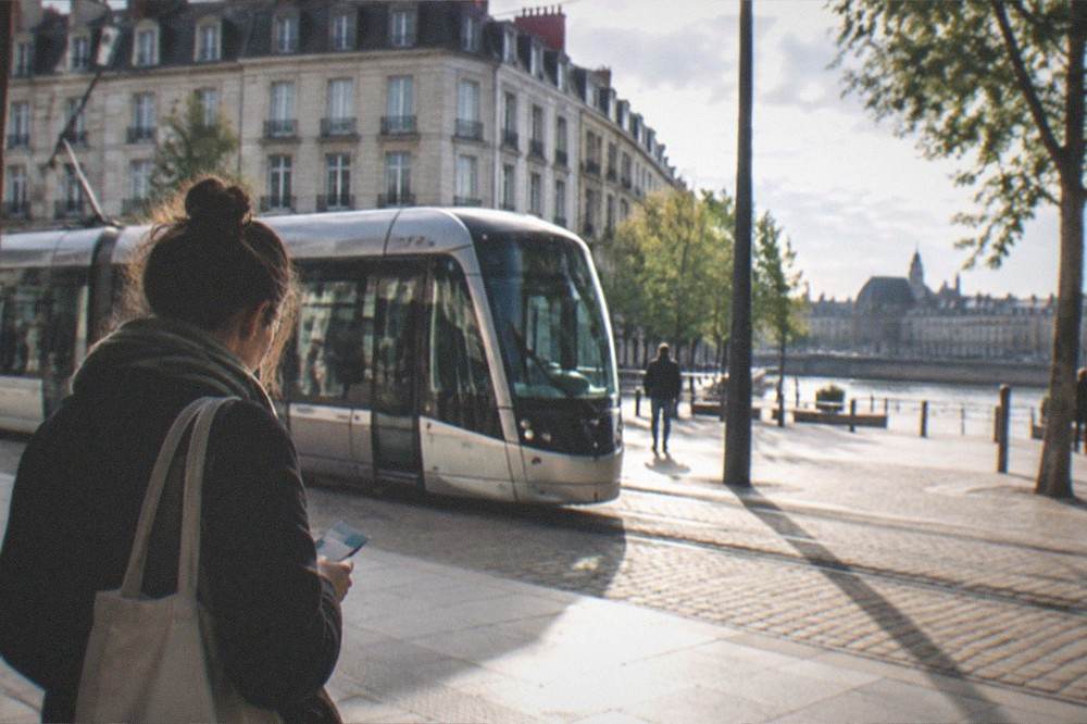A visitor holding a city pass beside a tram in Nantes on a sunny morning