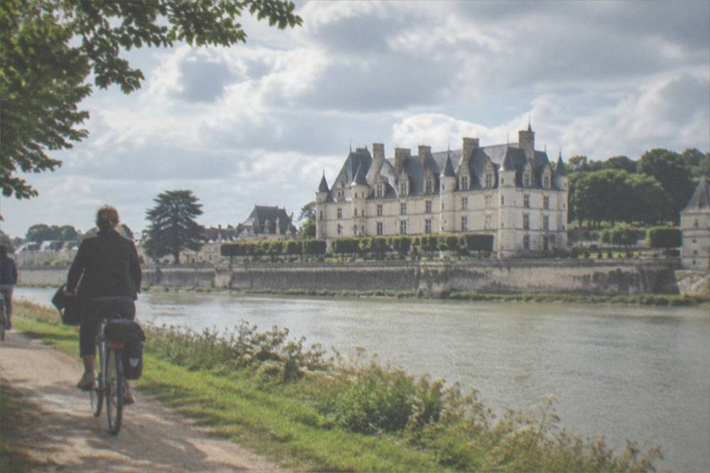 Cyclists riding a riverside path beside the Loire with a château in the distance