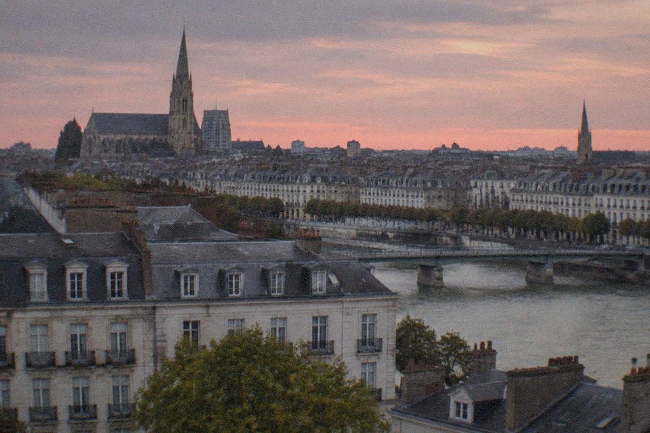 Evening view over Nantes rooftops and church spires under a soft pink sky