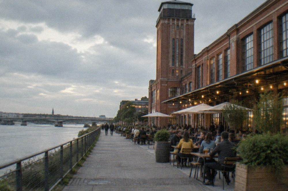 People drinking at outdoor tables along a lit warehouse promenade by the Loire at dusk