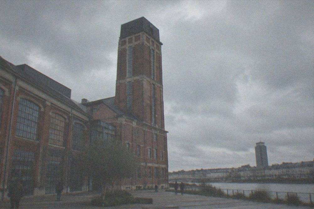 A tall office tower rising above low slate rooftops along a river