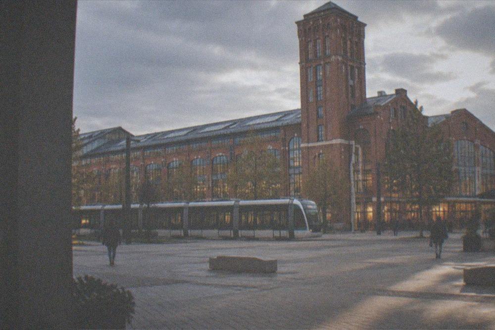 A modern tram gliding past lit shopfronts on a warm evening street