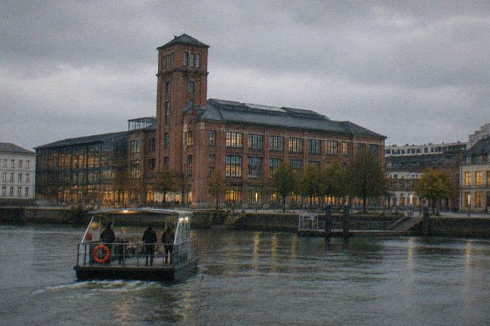 A small river ferry crossing dark water toward lit quayside buildings at night