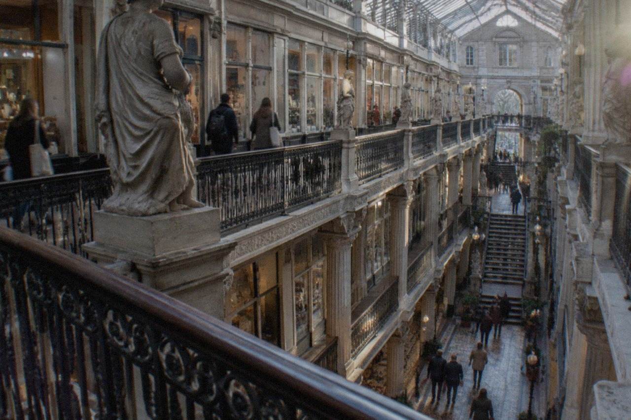 Shoppers walking under the glass roof and iron balconies of a nineteenth-century shopping arcade