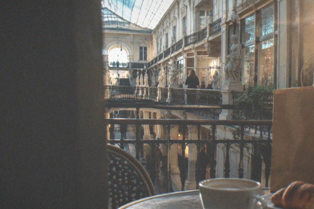 A cafe table with a coffee and a pastry beside a shopping bag on a city square
