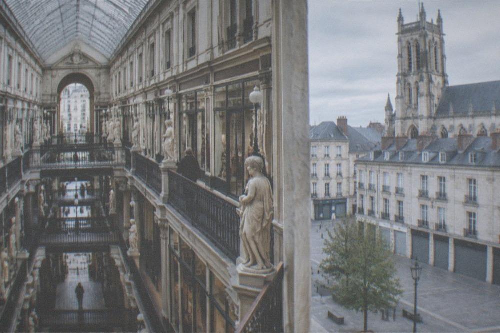 A quiet city square with closed shop shutters and a church tower in the morning light