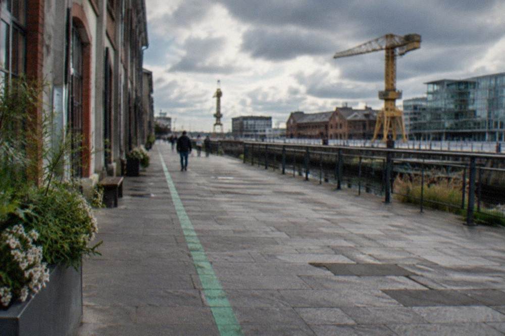 A green painted line running along a stone pavement past shops and old buildings