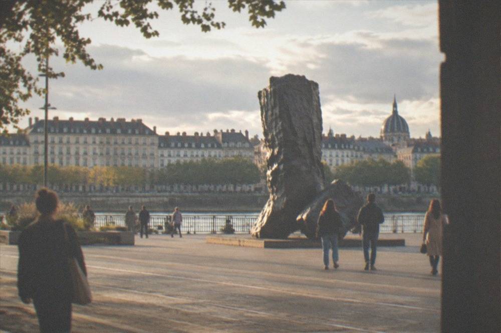 People strolling past a large outdoor sculpture on a sunny square in Nantes