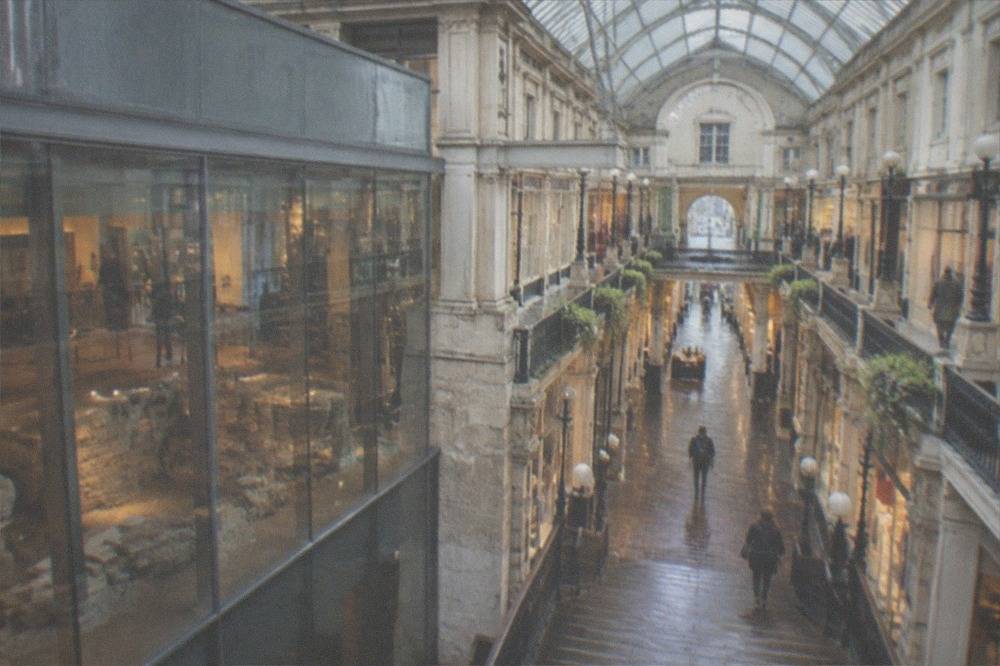 A monumental staircase inside a 19th-century glass-roofed shopping arcade lined with small boutiques