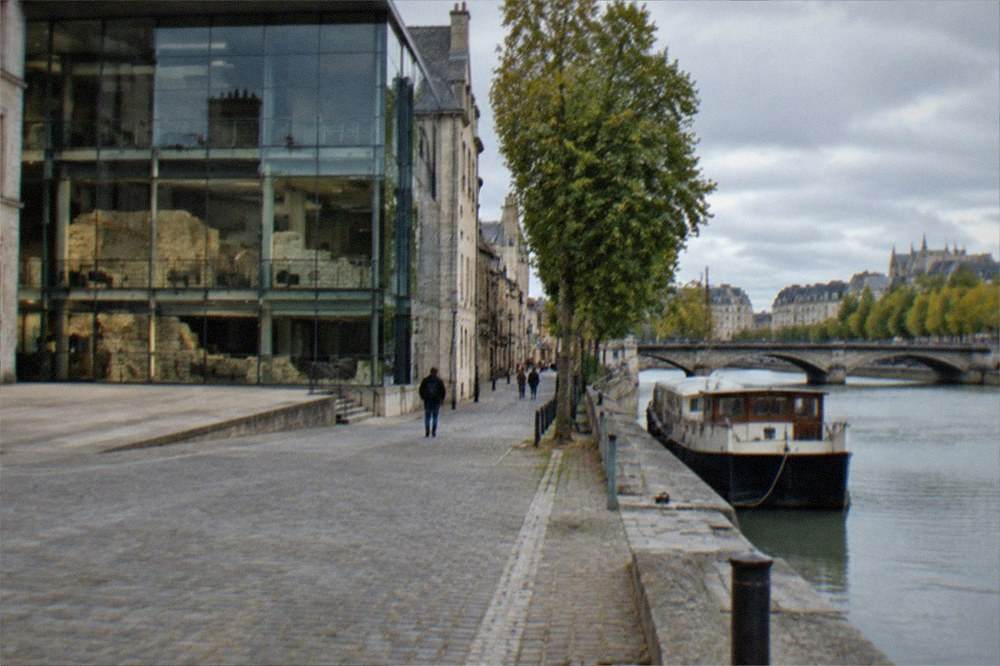 A river boat moored on a tree-lined riverbank near a stone bridge