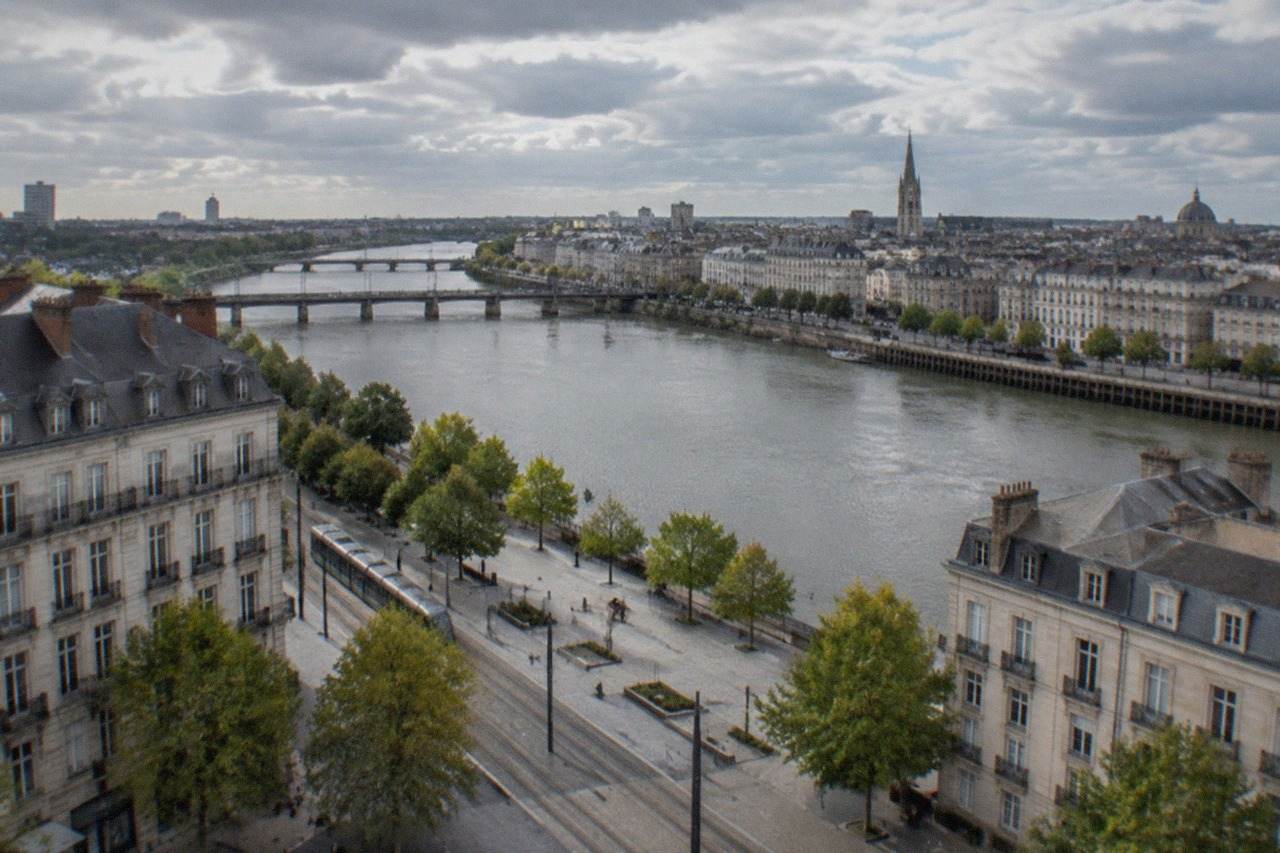 Wide view over the Loire river flowing through Nantes, with the city's rooftops and towers under a partly cloudy sky
