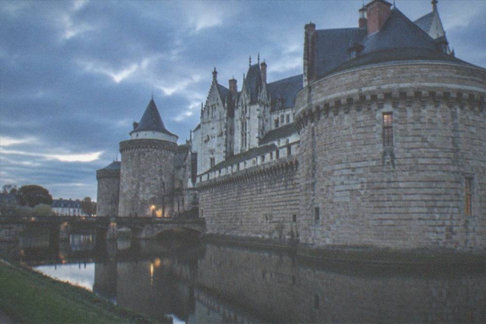 The stone ramparts and towers of the Château des ducs de Bretagne reflected in the moat at dusk