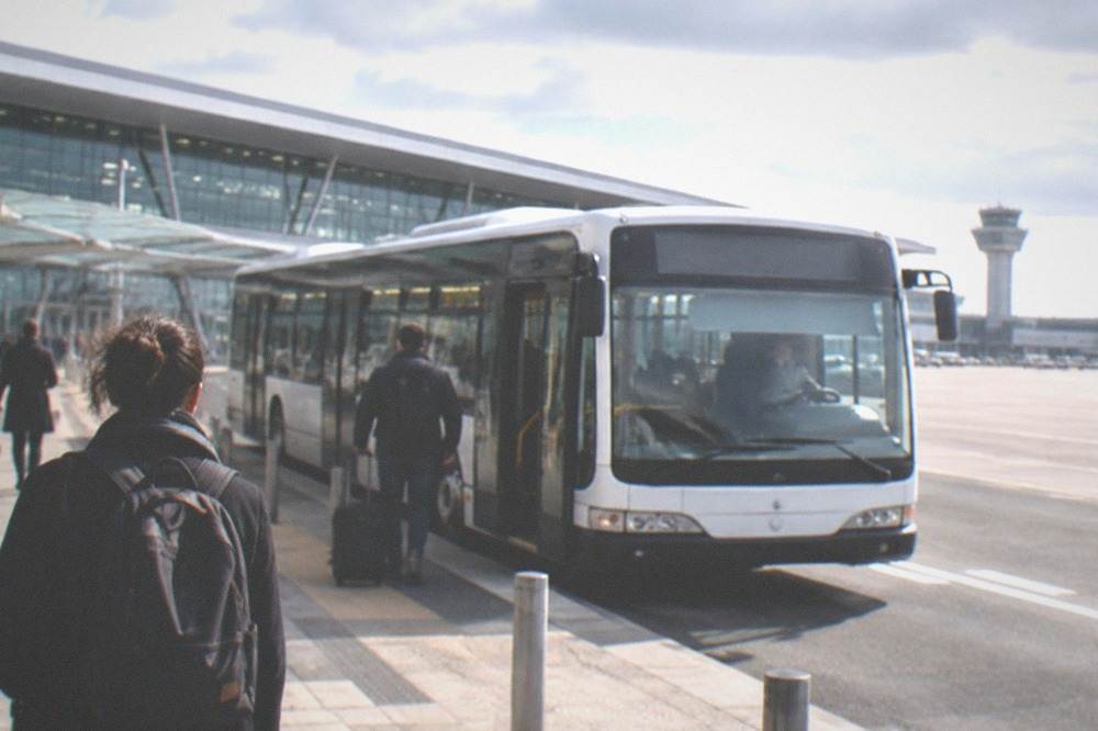 An airport terminal forecourt with a shuttle bus waiting at the kerb in morning light