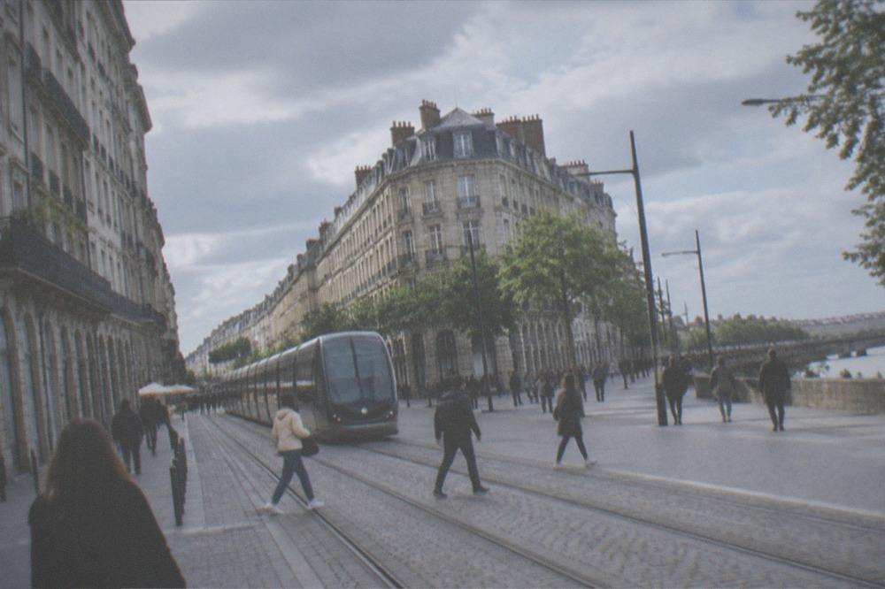 A busy tram street in central Nantes with pedestrians crossing between stone buildings