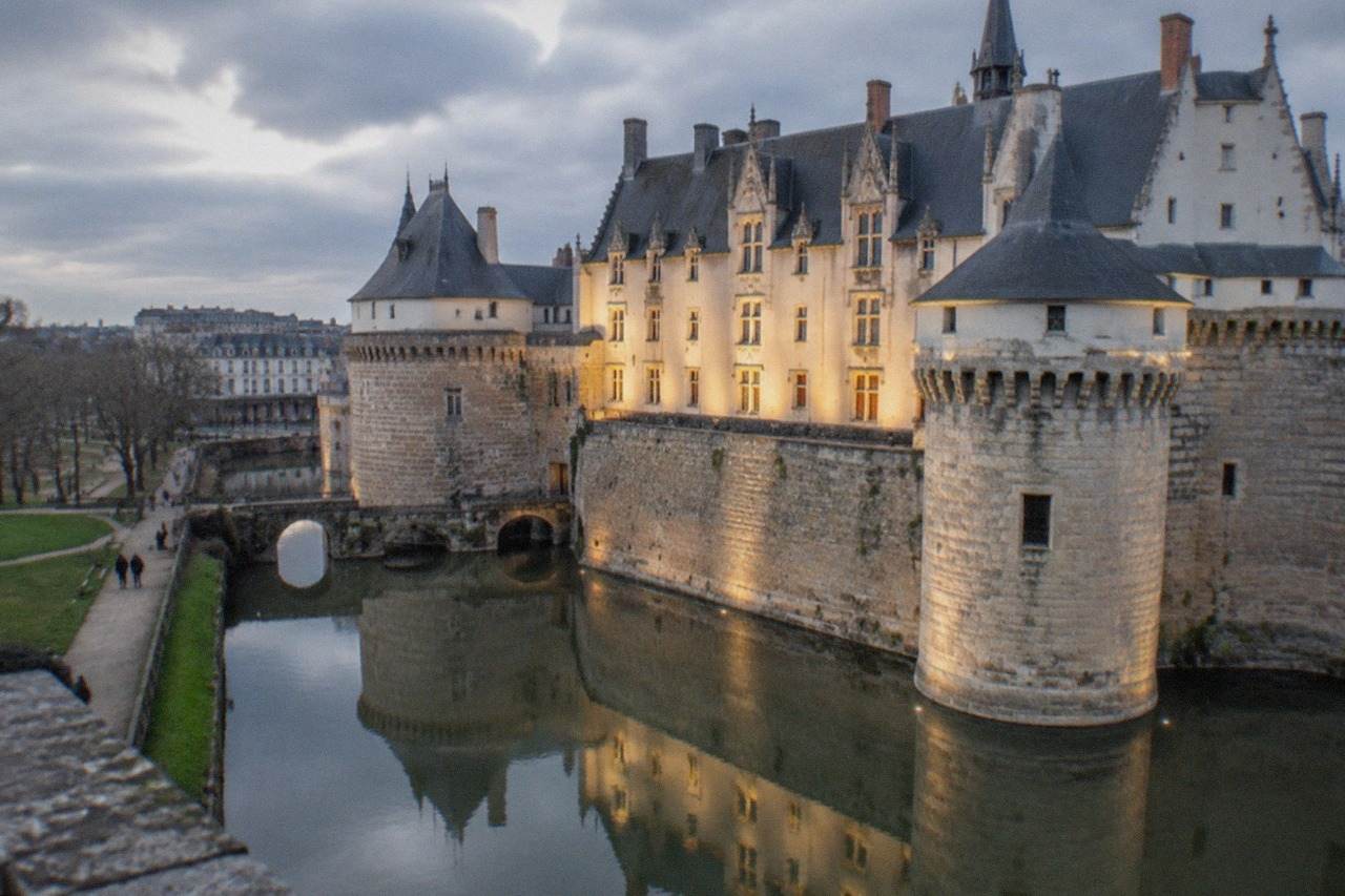 The floodlit facade of the Château des ducs de Bretagne reflected in its moat at dusk