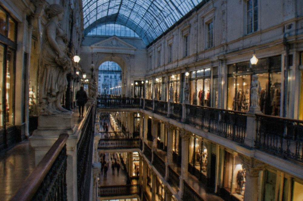 The illuminated glass roof and shopfronts inside the Passage Pommeraye shopping gallery in the evening