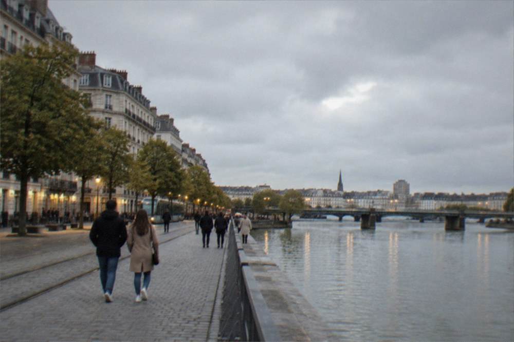 People strolling along the Quai de la Fosse in Nantes with the lit riverfront and bridge behind them
