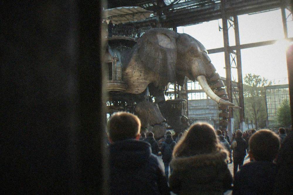 Children watching a large mechanical elephant machine in an industrial workshop hall