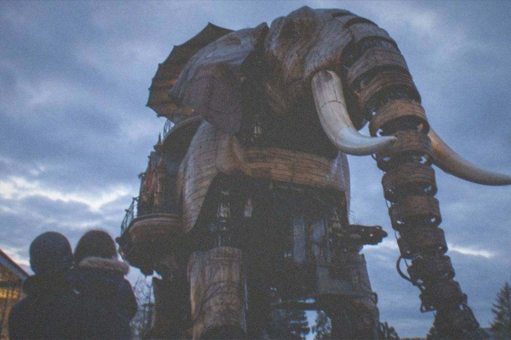A parent and child looking up at a tall mechanical elephant machine outdoors on a former shipyard site