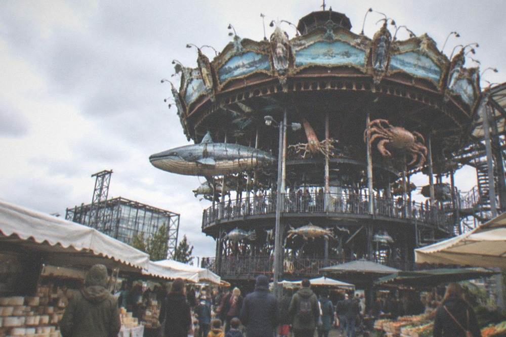 A busy open-air food market with families browsing stalls of cheese and produce