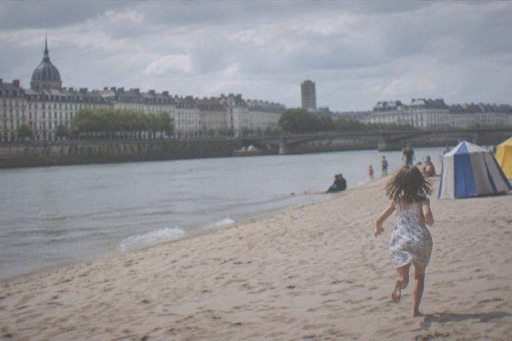 A child running along a wide sandy beach near colourful beach tents