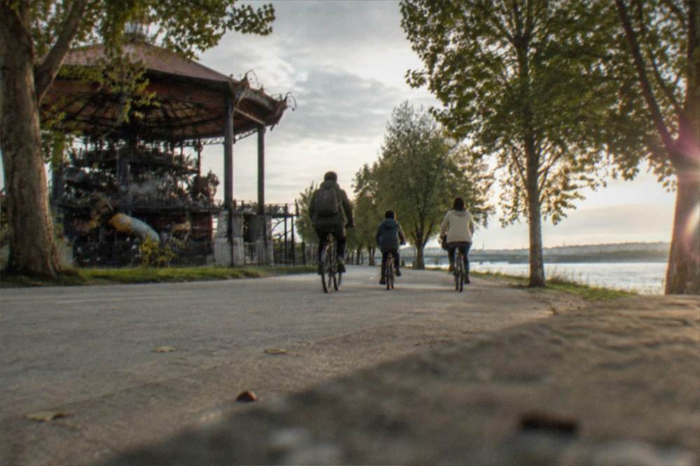 A family cycling together on a riverside path with trees on both sides