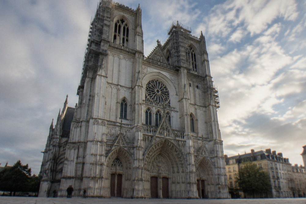The white stone facade of Nantes Cathedral seen from the square, with scaffolding on the towers