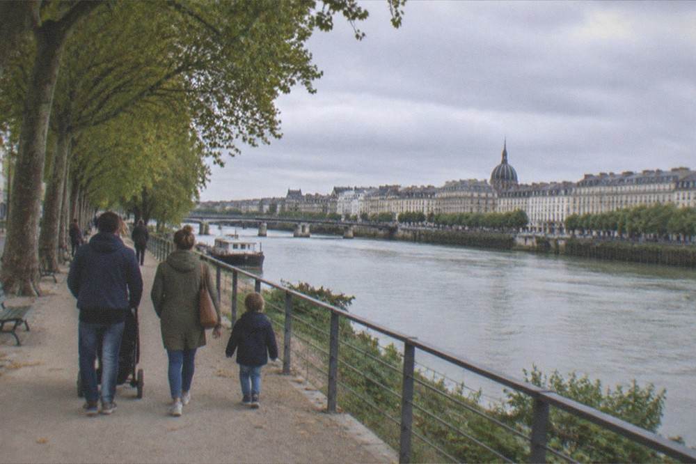 A family walking a riverside promenade under plane trees in Nantes