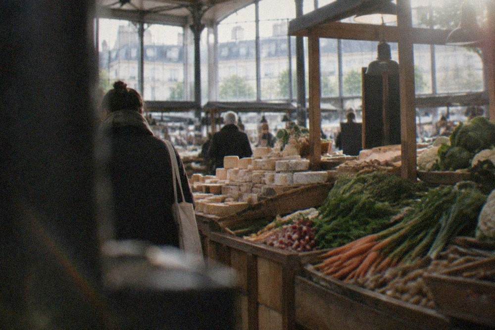 A wooden market stall piled with vegetables and cheeses at an indoor market in Nantes
