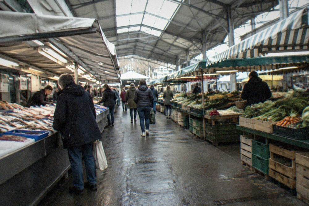 Customers browsing a covered food market aisle with fish and produce stalls
