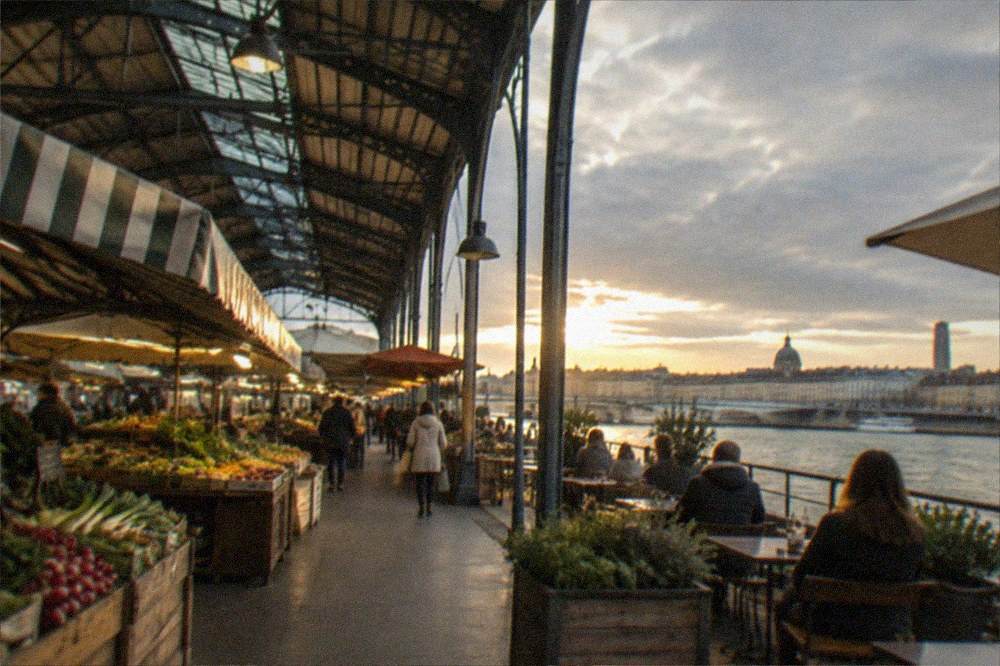 A riverside terrace with diners looking across the water at a French city skyline